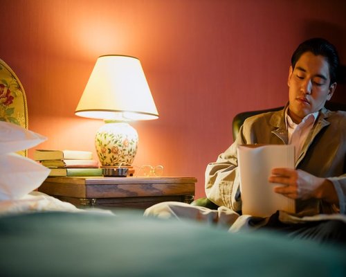 A person reading a book in bed with a warm glowing table lamp beside them