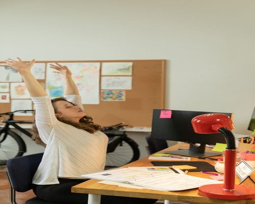 A person stretching their arms backwards while sitting at a desk, taking a short break from the computer